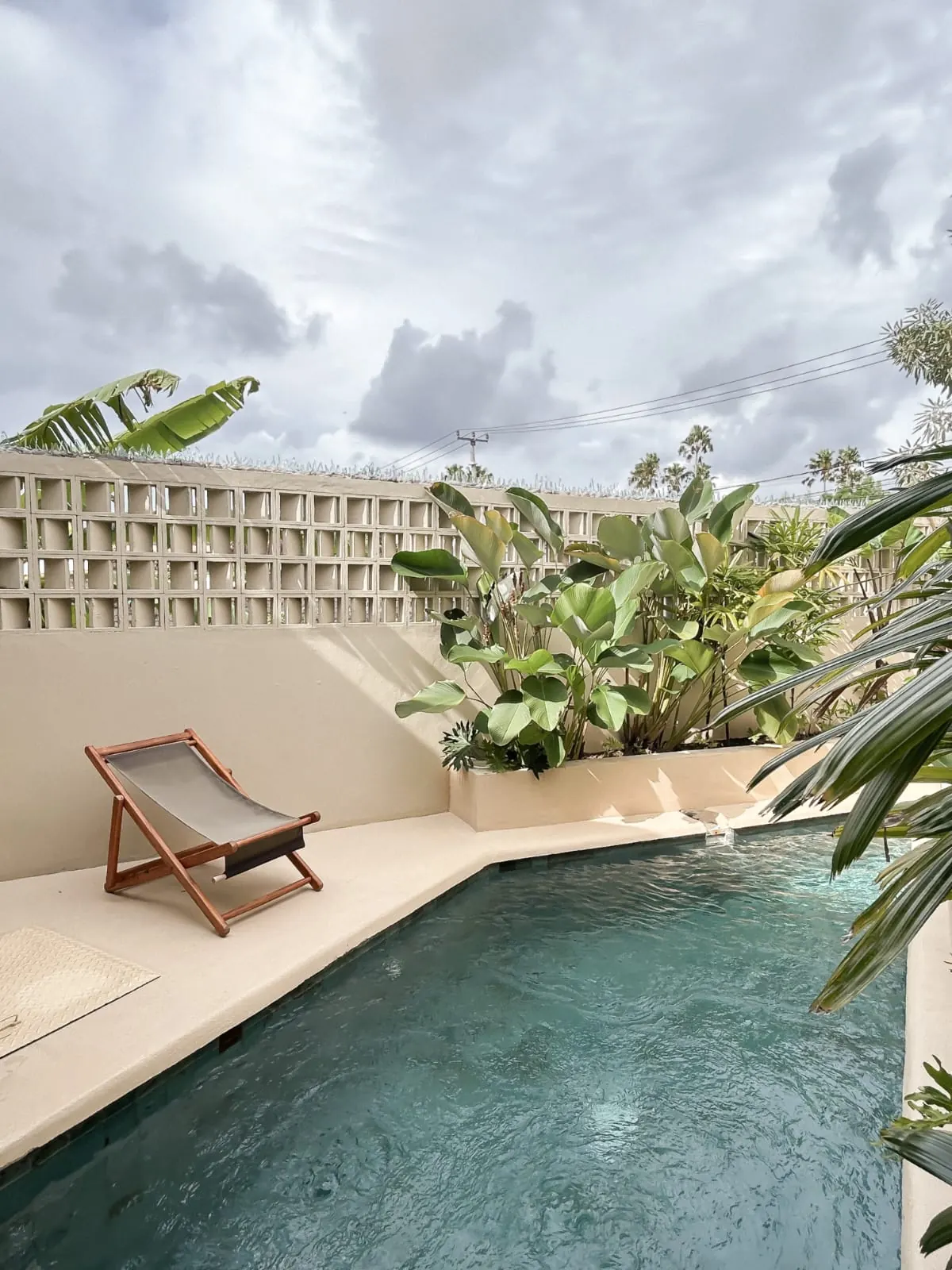 Private plunge pool with breeze-block wall, tropical plants and sling chair